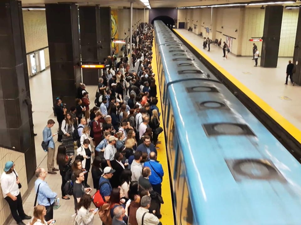 Des usagers sur un quai du métro de Montréal, alors que le train arrive en station.