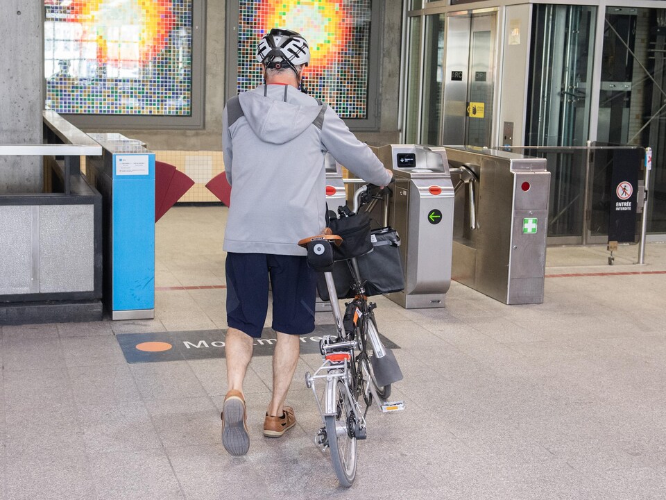 Un homme fait passer sa bicyclette dans un tourniquet à l'intérieur d'une station de métro à Montréal.