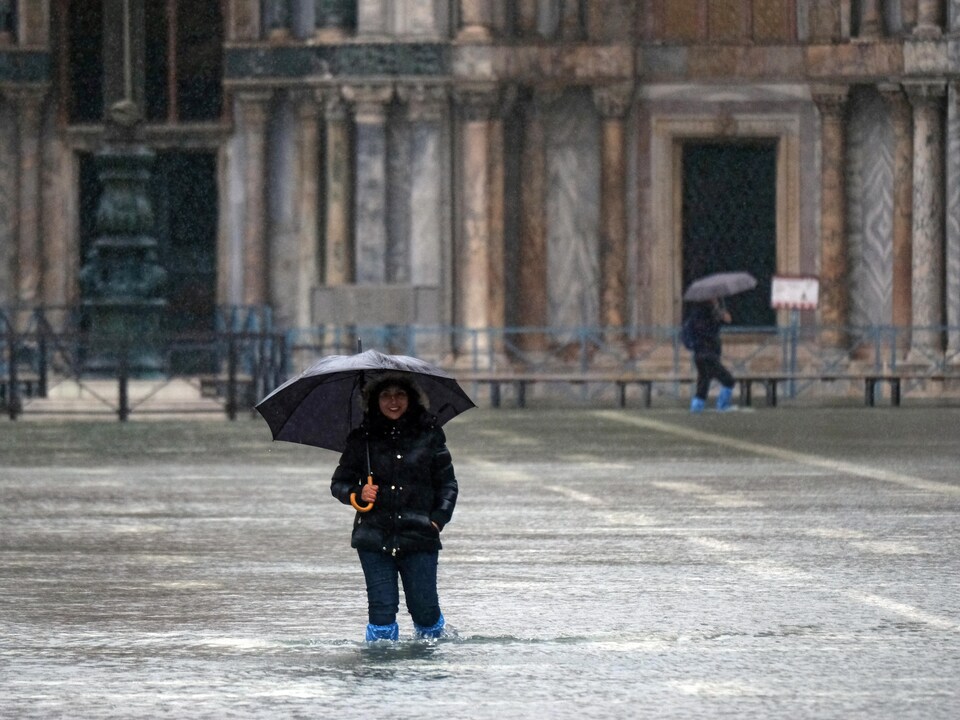 Une touriste se tient sur la place Saint-Marc à Venise, avec un parapluie et de l'eau jusqu'aux genoux.