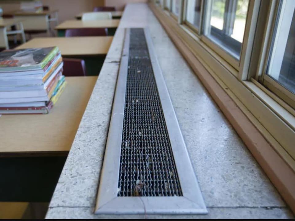 Une pile de livres sur un pupitre près de fenêtres dans une classe.