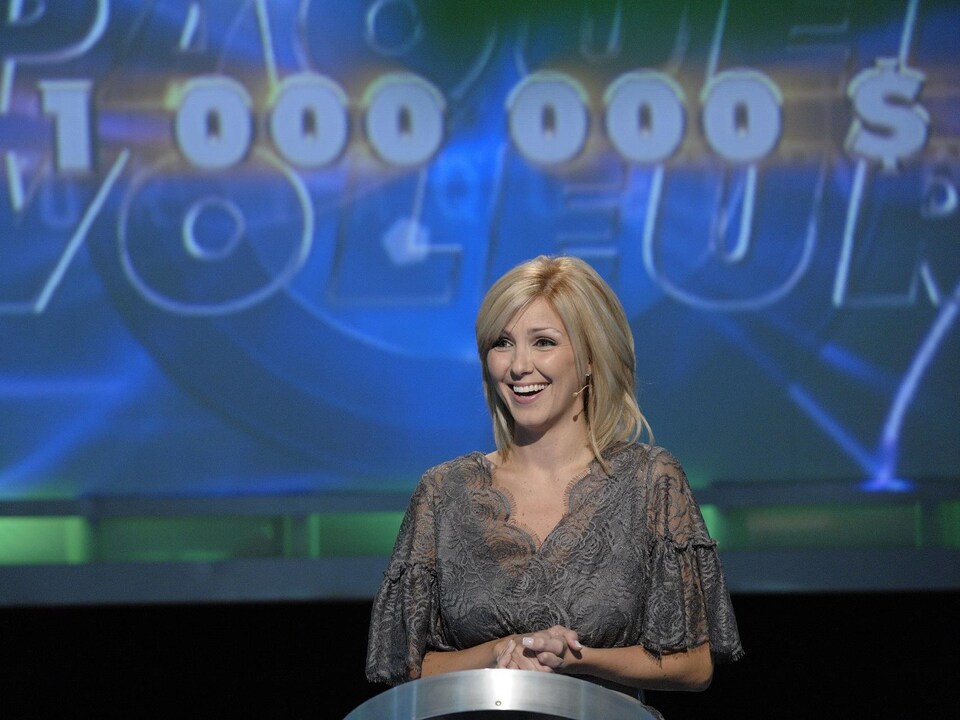 Véronique Cloutier à son lutrin dans le studio du jeu-questionnaire en 2008. Derrière elle, un écran géant affiche le montant de 1 million de dollars.