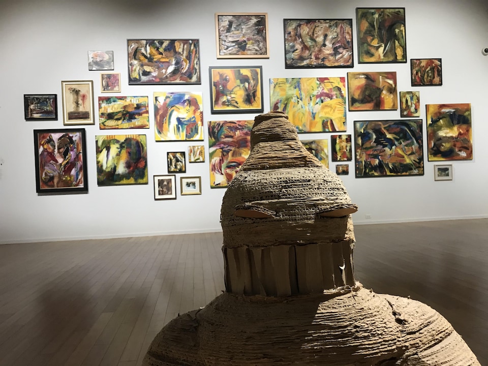 Une sculpture en premier plan, des tableaux accrochés au mur en arrière-plan.