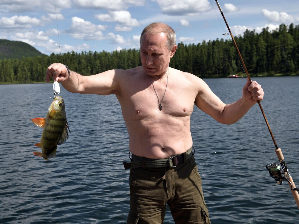 Le président russe, Vladimir Poutine, torse nu au bord d'un lac, un poisson et une canne à pêche à la main.