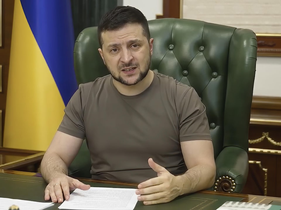 Vêtu d'un t-shirt kaki, Volodymyr Zelensky est assis sur un fauteuil vert derrière son bureau. 