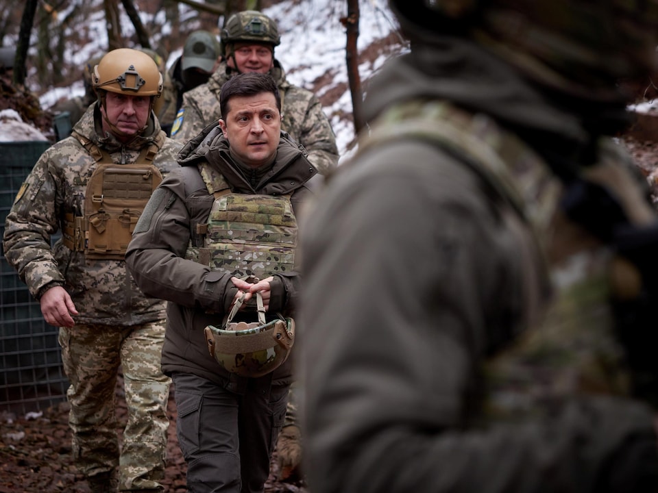 En habit de combat, Volodymyr Zelensky marche dans un boisé enneigé avec des soldats.
