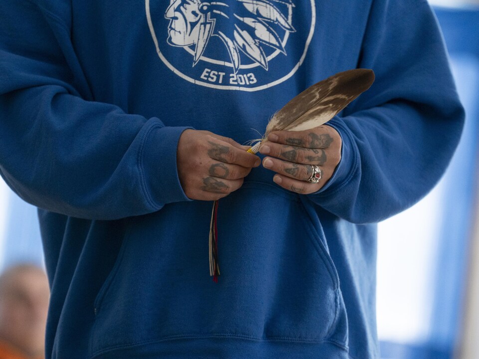 Un homme dont on ne voit pas le visage qui tient dans ses mains une plume d'aigle.
