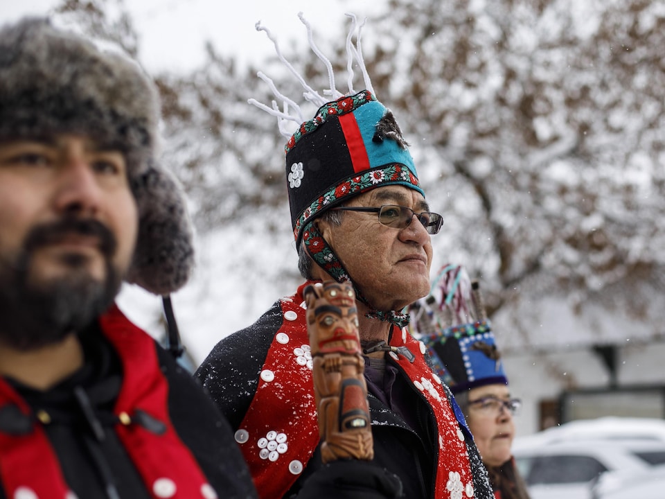 Trois chefs autochtones portant des tenues traditionnelles marchent dans une rue enneigée.