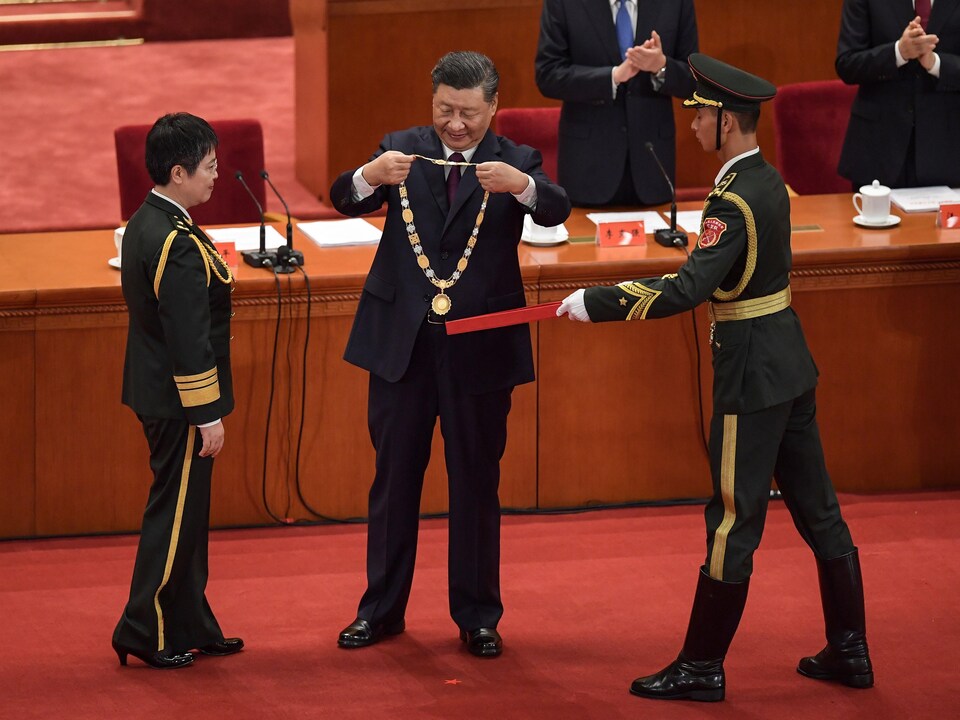 M. Xi tient une médaille dans ses mains une médaille qu'il s'apprête à passer au cou de la générale.