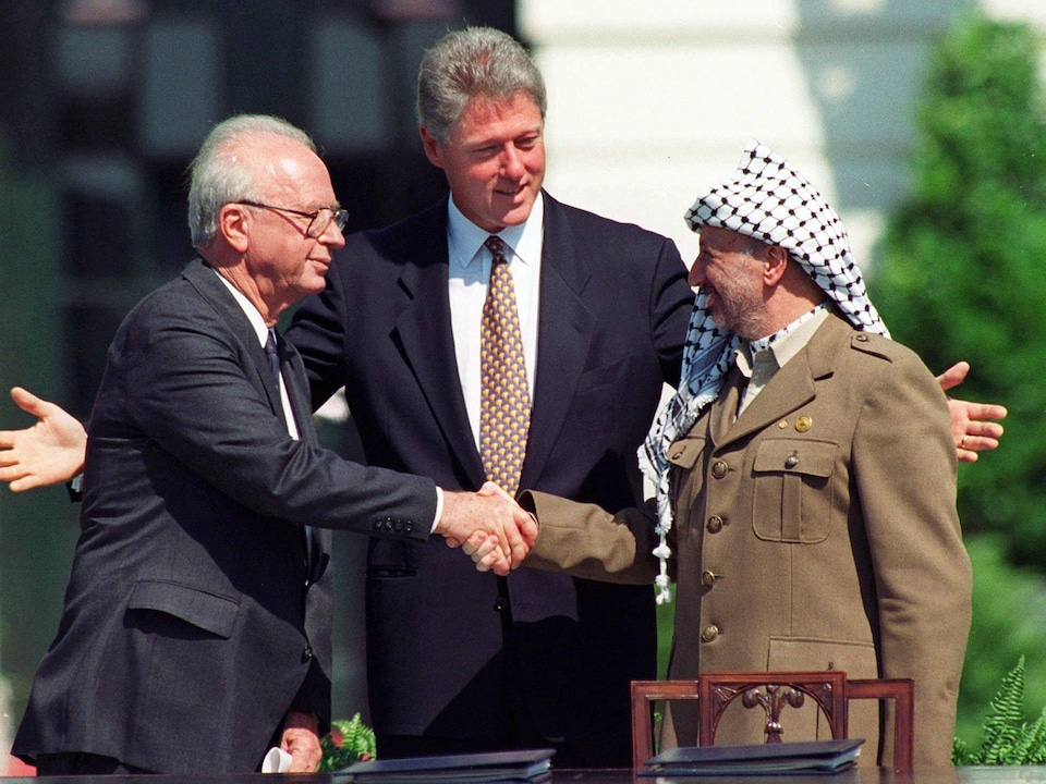 Deux hommes se serrent la main devant Bill Clinton.