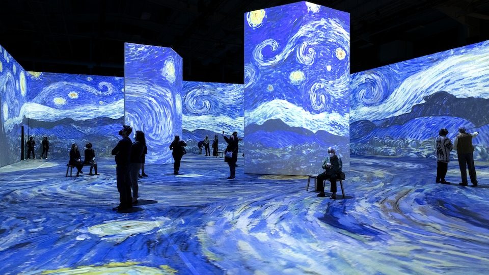 Des personnes dans une salle dans laquelle sont projetées des toiles de l'artiste Van Gogh. 