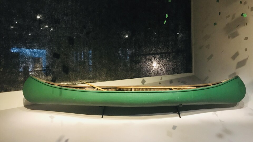 Un canot vert, assez vieux, dans une salle d'exposition.