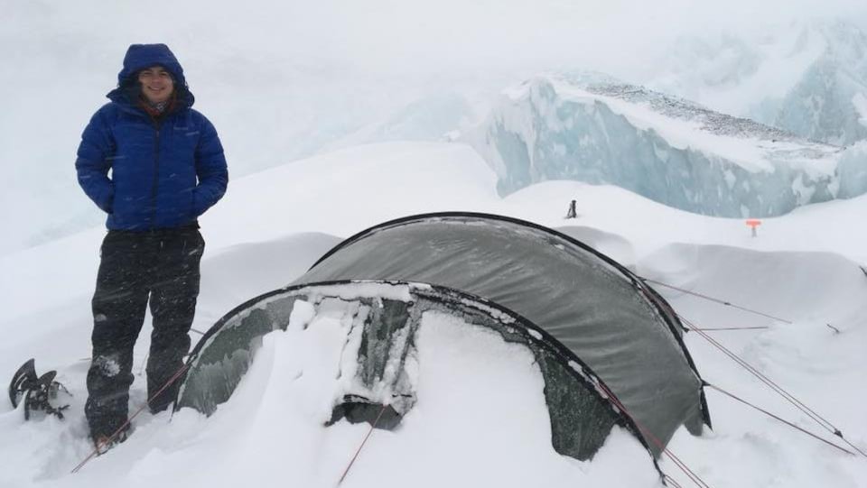 Jean-François est debout à côté de sa tente dans une tempête de neige.