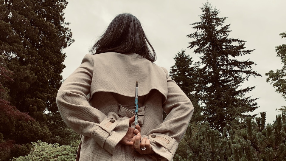 Femme de dos qui tient un pinceau entre ses mains.