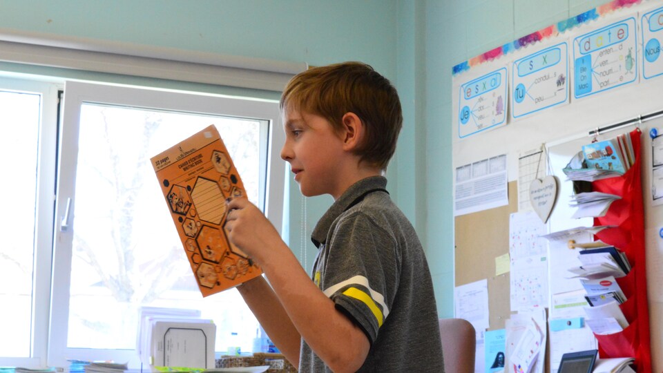 Un enfant lit les phrases qu'il a rédigées dans son cahier.