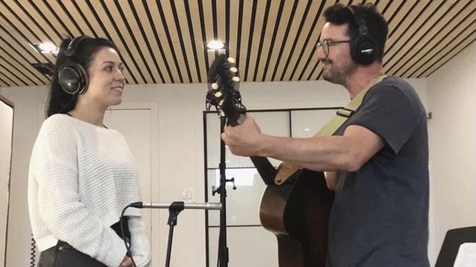 Un homme avec une guitare chante en duo avec une femme devant lui. 