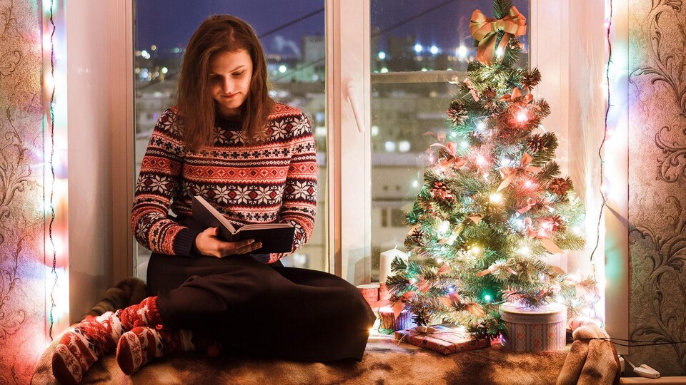 Une jeune femme lit un roman dans un décor de Noël. 