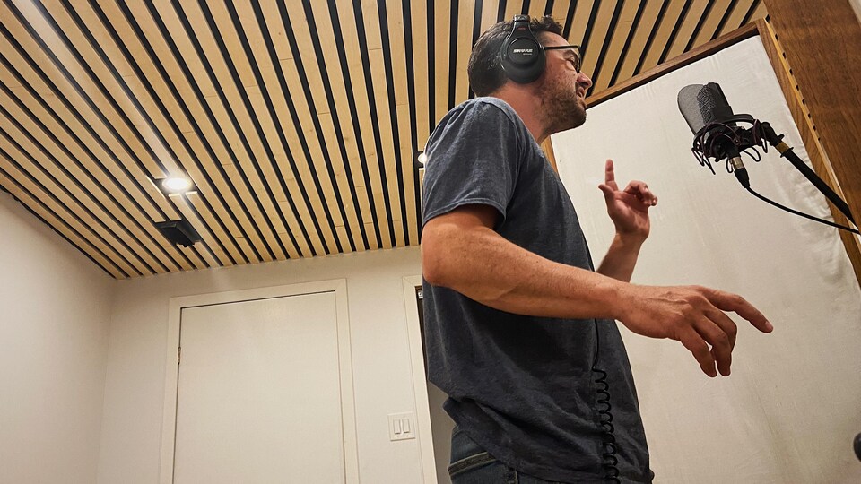 Un homme chante devant un micro dans un studio d'enregistrement. 