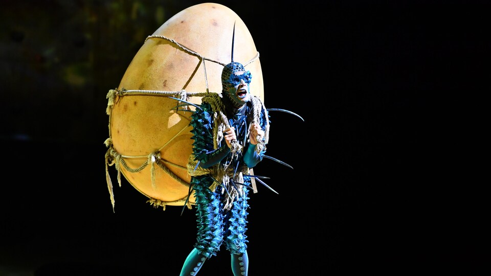 Une personne déguisée en mouche avec un œuf immense sur son dos. 