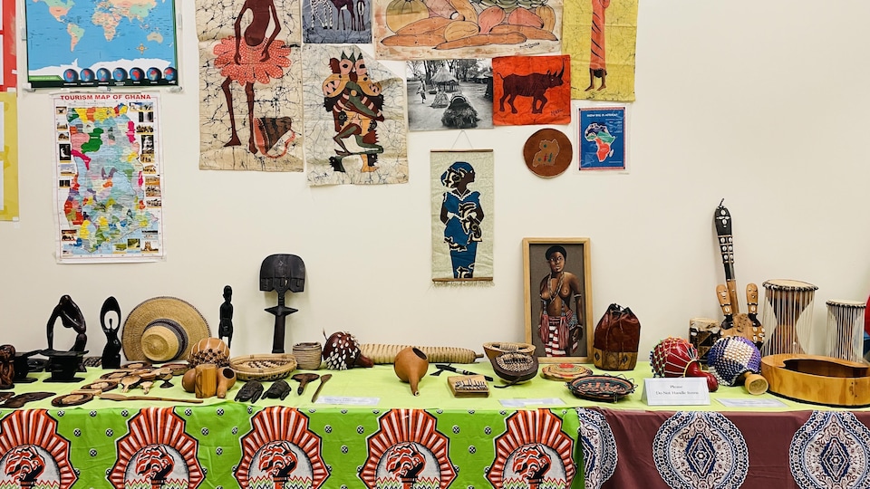 Table sur laquelle sont posés des instruments de musique et des sculptures en bois. Au mur, des affiches et des images représentant des fruits et une carte de l'Afrique. 