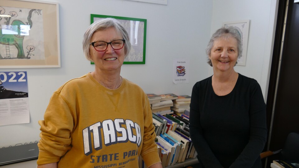 Deux femmes sourient devant une pile de livres.
