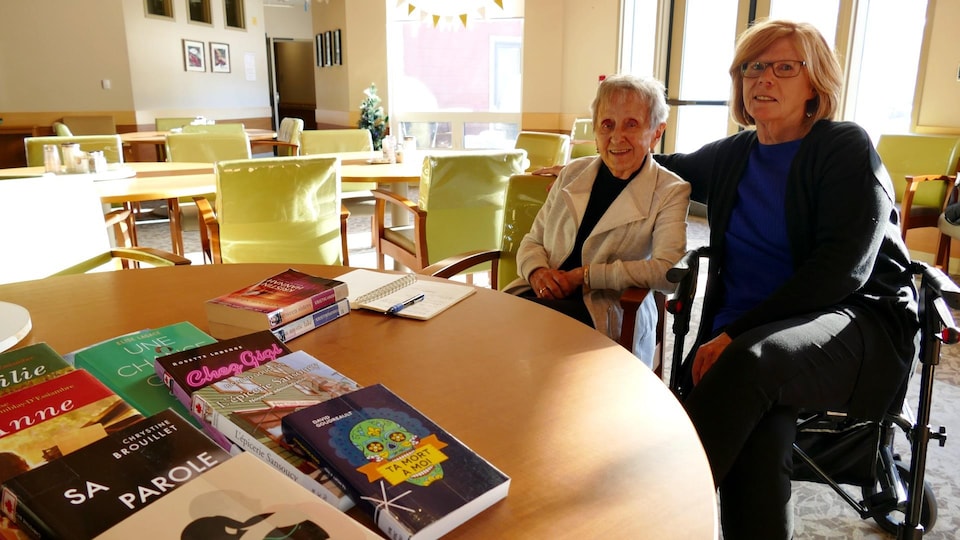 Deux femmes assises à une table sur laquelle sont posés des livres.
