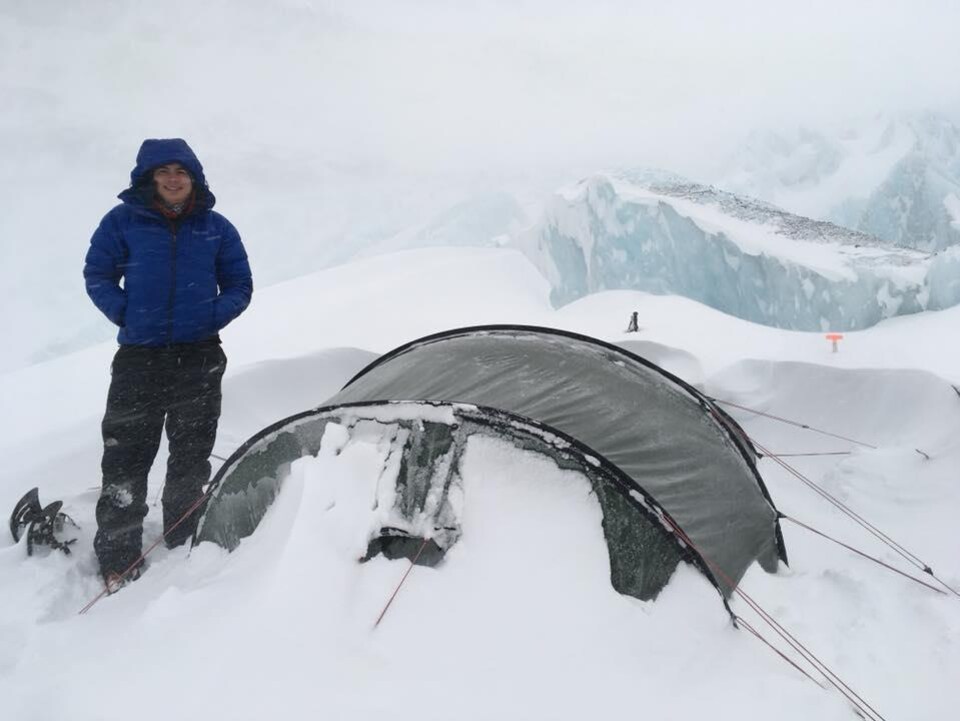 Jean-François est debout à côté de sa tente dans une tempête de neige.