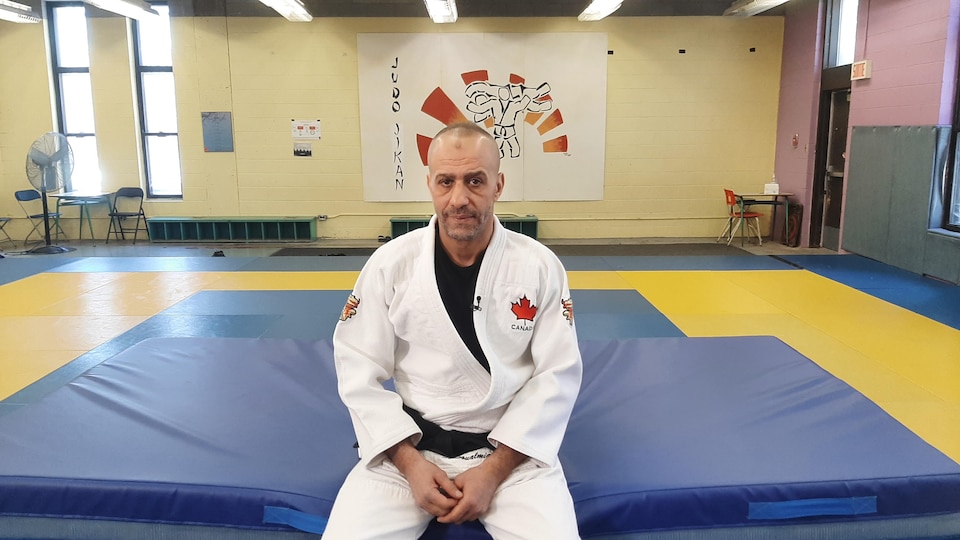 A man kneeling on a mat with a white judoji looking at the camera