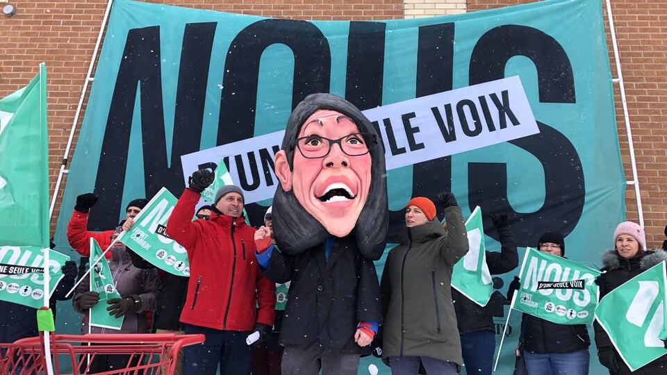 Des manifestants tiennent une tête géante de papier mâché. 
