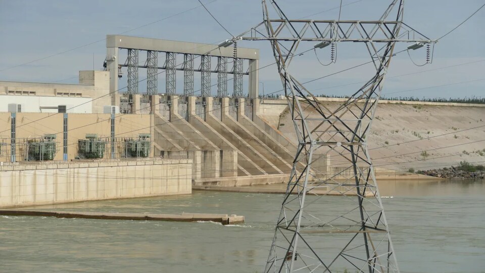Un pylône électrique devant un barrage hydroélectrique.