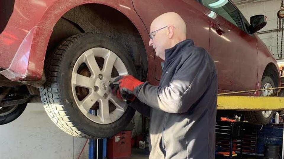 Jano Roussel installe un pneu sur un véhicule dans son garage.