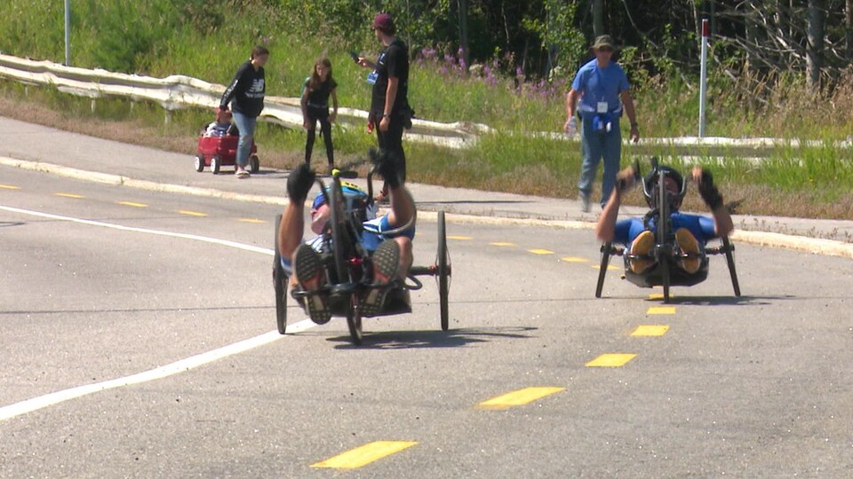 Des paracyclistes sont sur une piste à l'extérieur. 