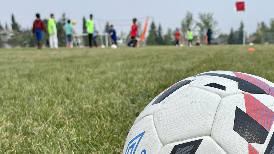 Un ballon de soccer avec en arrière-plan des enfants qui jouent.