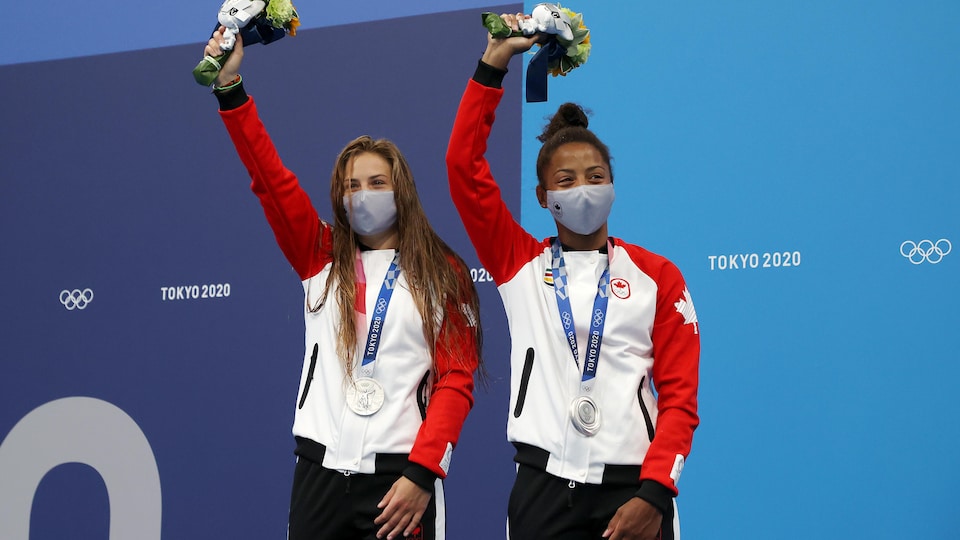 Mélissa Citrini-Beaulieu et Jennifer Abel célèbrent leur médaille d'argent au cou, le bras droit au ciel et un bouquet à la main, sur la deuxième marche du podium.