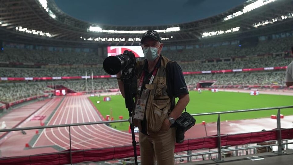 Bernard Brault tient un appareil photo et un trépied dans le stade olympique de Tokyo.