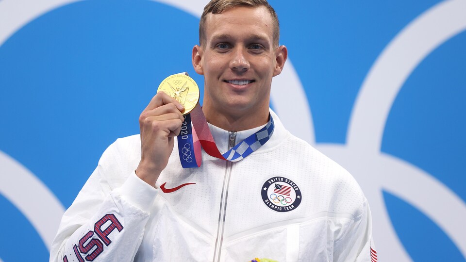 Il porte un manteau aux couleurs des États-Unis et montre fièrement sa médaille d'or. 