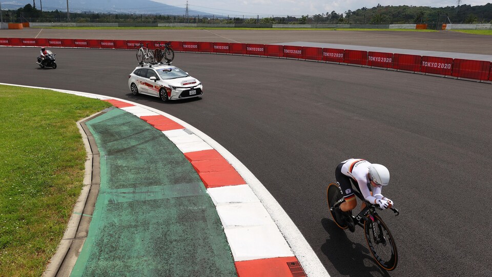 Il roule sur un circuit dans un contre-la-montre et la voiture d'équipe la suit.