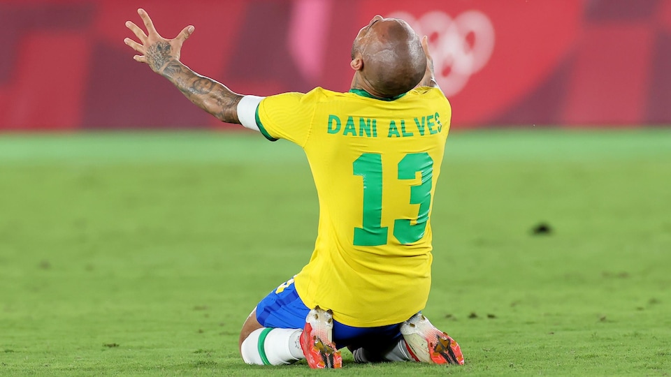 Dani Alves ajoelhado em campo comemora a vitória.