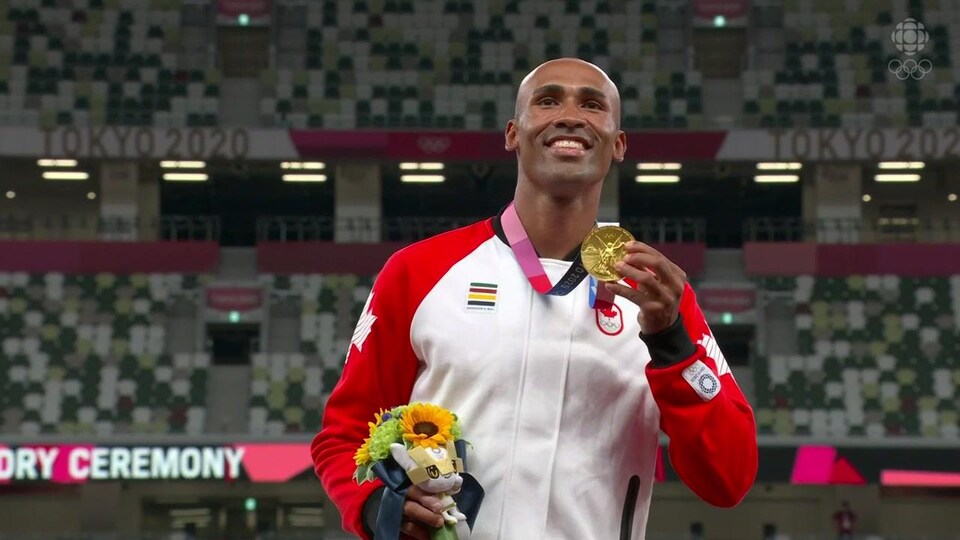 Damian Warner sourit en tenant sa médaille d'or.