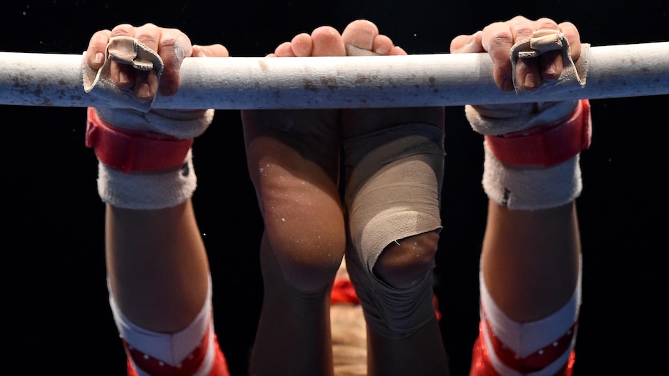 Image rapprochée sur mains et pieds d'une gymnaste qui tient une barre­.