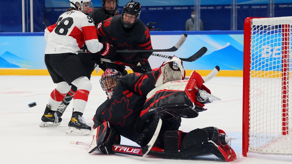 Une gardienne de hockey est sur la patinoire et lève ses deux jambières pour faire un arrêt pendant un match olympique.