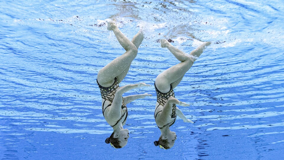 Les deux nageuses artistiques sont sous l'eau, la tête en bas.