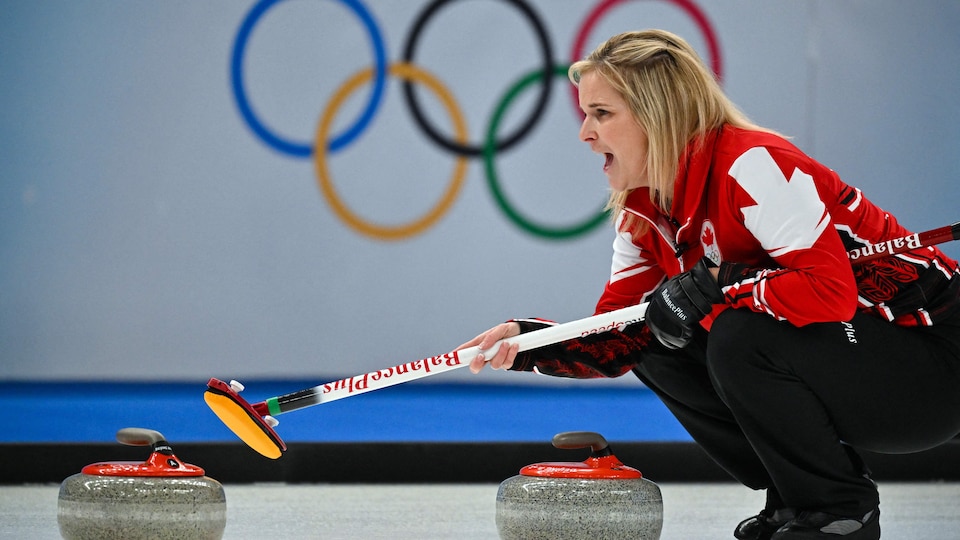 Jennifer Jones penchée vers les pierres de curling et qui regarde au loin pour donner des directives à ses coéquipières. 