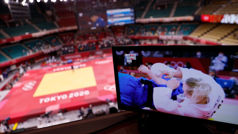 Dans un amphithéâtre, un écran de télé montre un combat de judo.