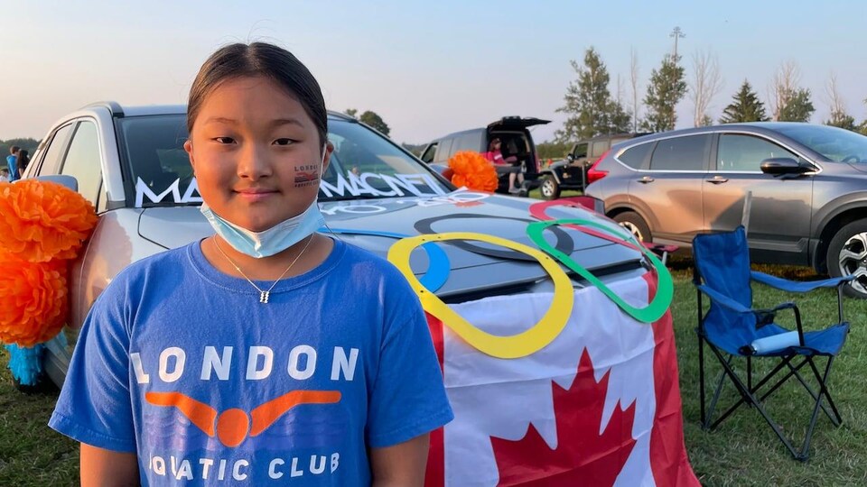 Kaitlyn Chen devant un véhicule décoré avec des anneaux olympiques et un drapeau du Canada.