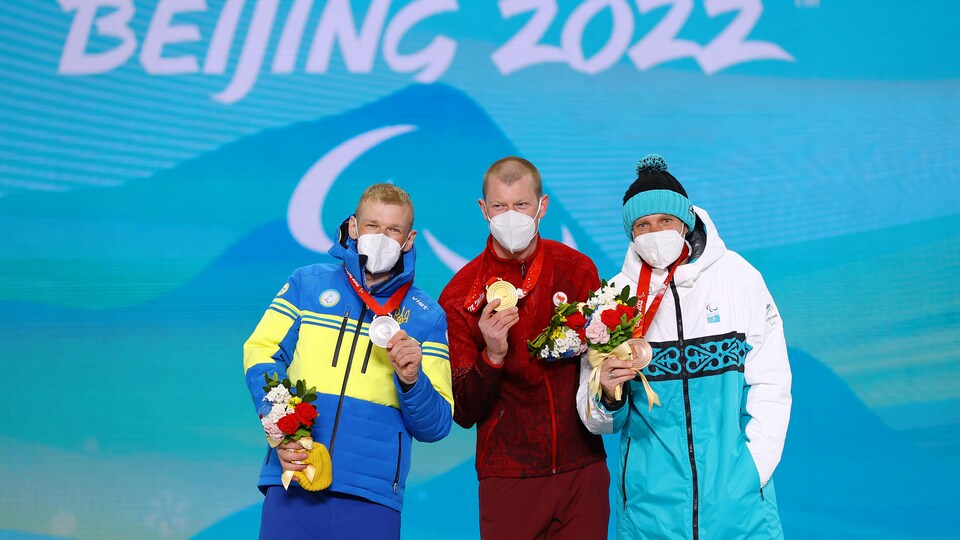 Trois athlètes paralympiques prennent la pose avec leurs médailles sur le podium.