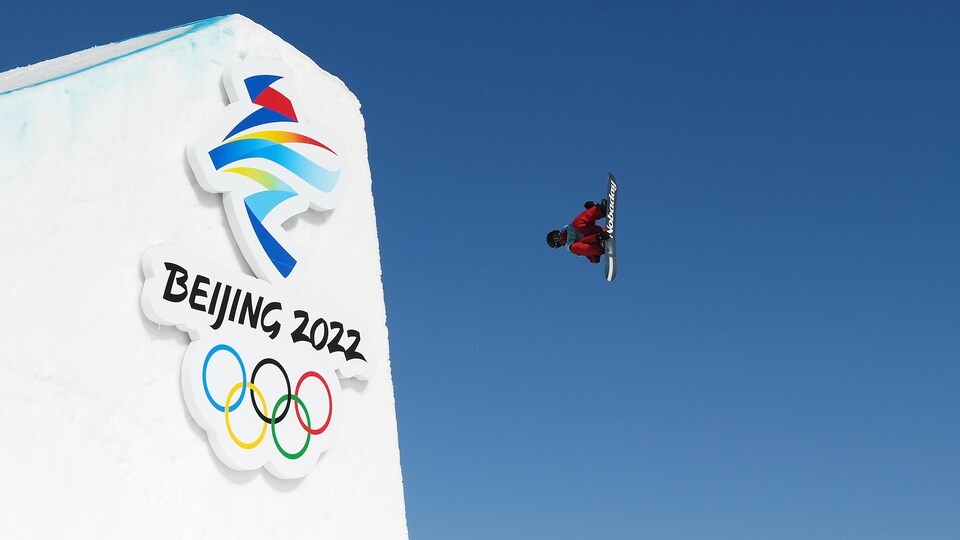 Au premier plan, la grande rampe qui porte le logo des Jeux olympiques de Pékin. Au second plan, Max Parrot, du Canada, exécute une figure dans les airs.