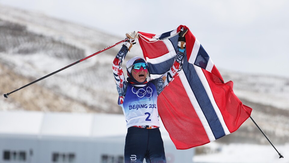 Une fondeuse lève le drapeau de la Norvège après avoir franchi le fil d'arrivée.
