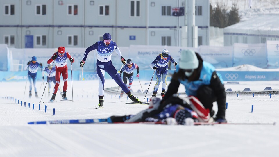 Une skieuse se trouve au sol, aidée par un entraîneur, pendant que ses adversaires arrivent au fil d'arrivée.