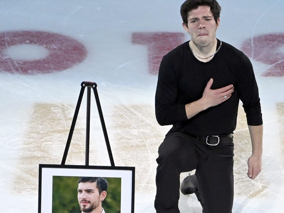 Un patineur canadien agenouillé sur la glace avec la main sur le cœur aux côtés d'une photo de son défunt frère.