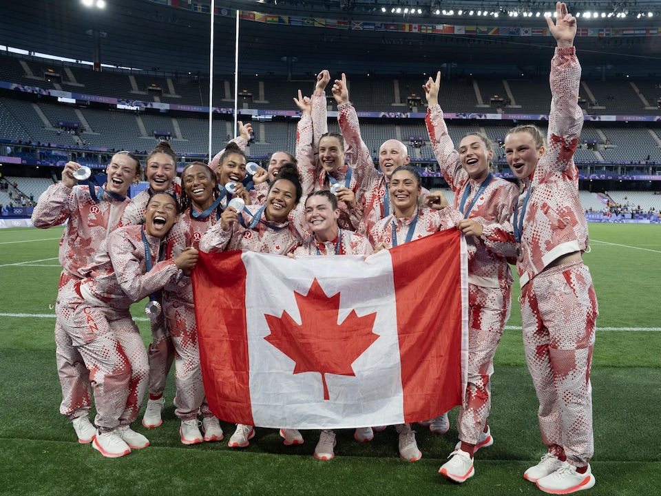 Les joueuses de l'équipe prennent une photo avec le drapeau canadien. 